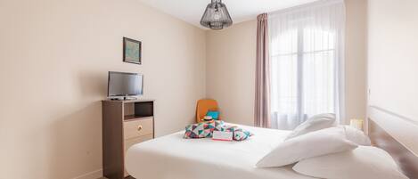 A hotel room with a bed, a TV on a wooden cabinet, a chair, and a window with curtains.