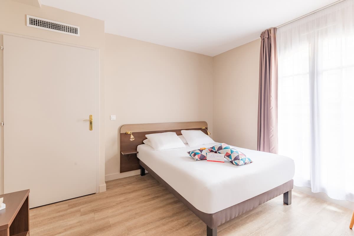 A hotel room with a bed, a bedside table, a wardrobe, and a window with curtains.