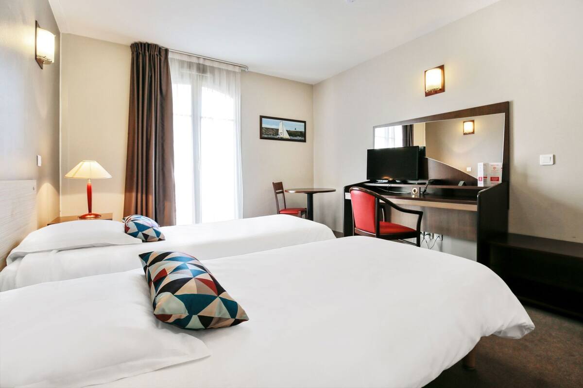A hotel room with two beds, a desk, a chair, a TV, and a large mirror.