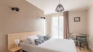 Habitación de hotel ordenada con una cama grande, mesita de noche, lámpara y una pequeña mesa con sillas.