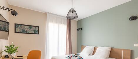 Habitación de hotel ordenada con una cama, un escritorio con una computadora portátil, una silla, una maleta y una planta.