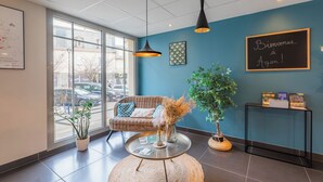 Un interior moderno con pared azul, sofá de mimbre, plantas en macetas y un cartel de bienvenida.