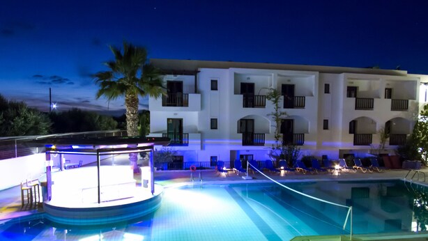 Un espace piscine d’hôtel doté d’une terrasse circulaire, de palmiers et d’un bâtiment avec des balcons.