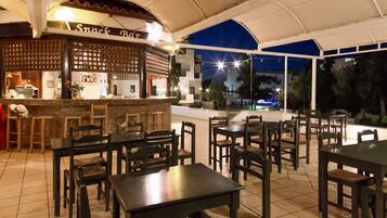 An outdoor restaurant with a bar area, multiple tables and chairs, and a view of the night sky.