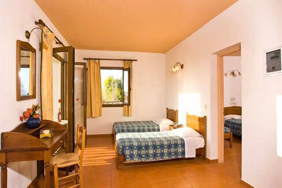 A room with two beds, a desk, a chair, a mirror, and a window with curtains.