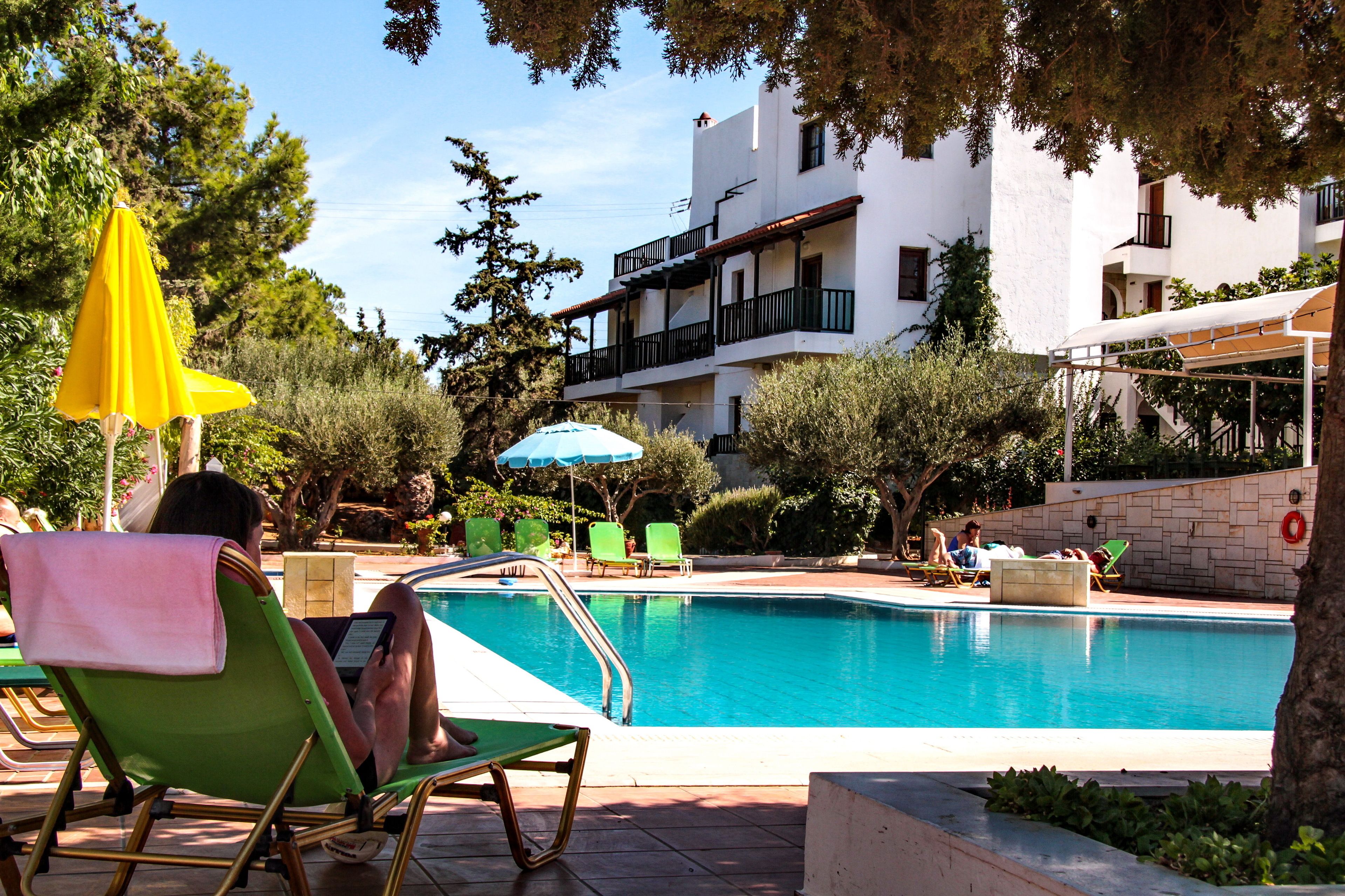 Zona de piscina con sillones de descanso, una sombrilla amarilla y un edificio con balcones.