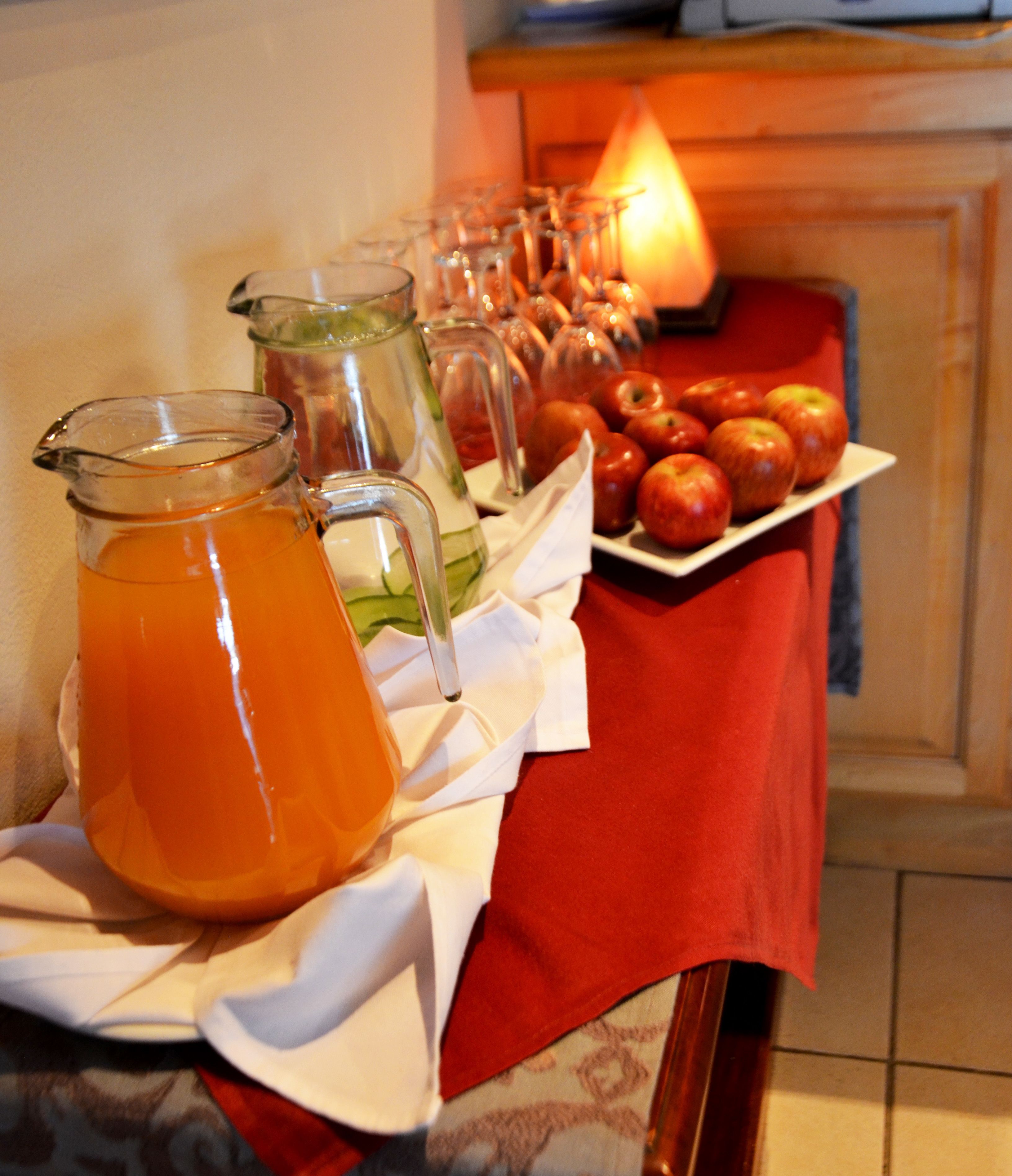 A table with a pitcher of orange juice, a glass pitcher, and a plate of apples.
