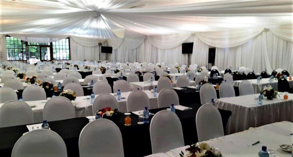 Un salón de banquetes con mesas redondas, sillas blancas y cortinas blancas drapeadas.
