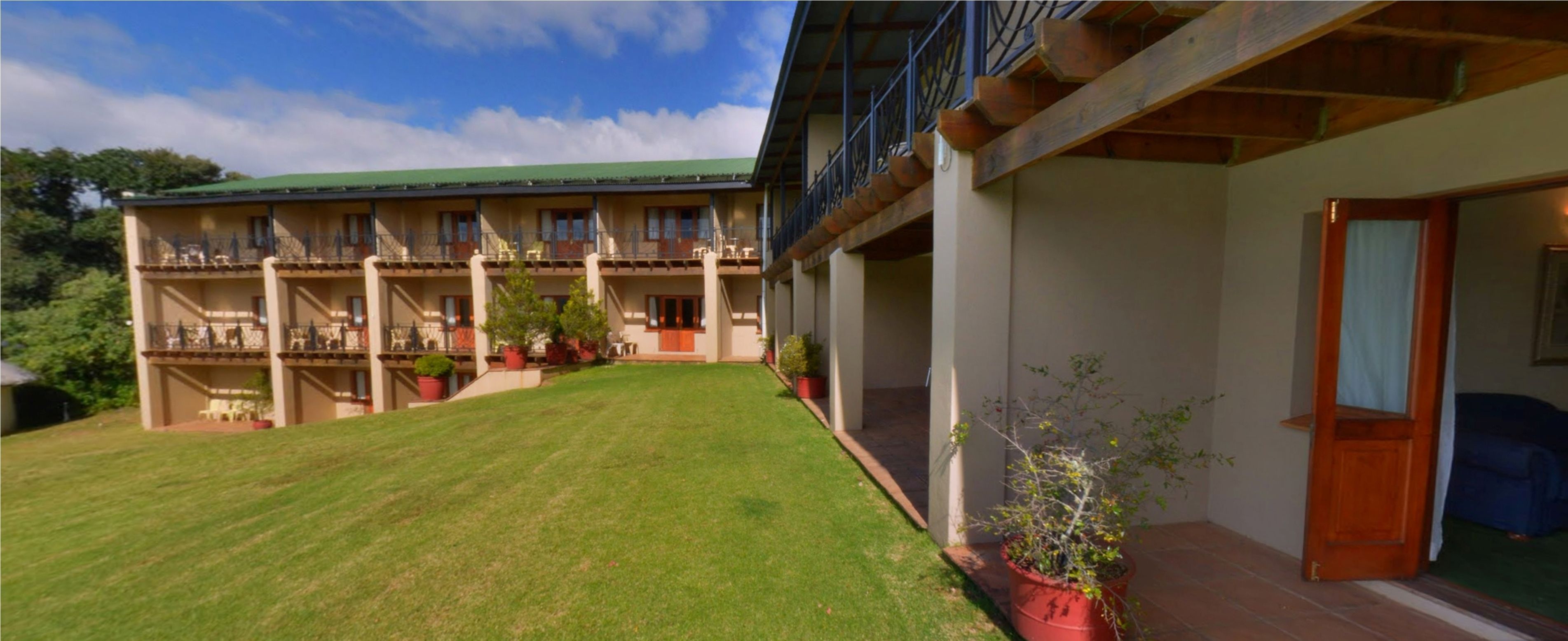 A two-story building with a green roof, multiple balconies, and a well-maintained lawn.