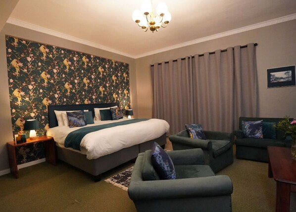 A bedroom with a bed, two armchairs, a sofa, a nightstand, a lamp, and a chandelier. - Magoebaskloof Hotel Tzaneen (Tzaneen)