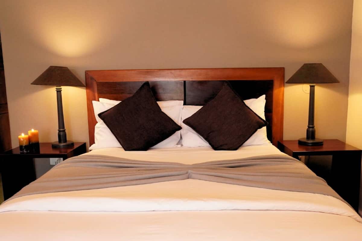 A neatly made bed with a wooden headboard, two bedside lamps, and two lit candles on the nightstands.