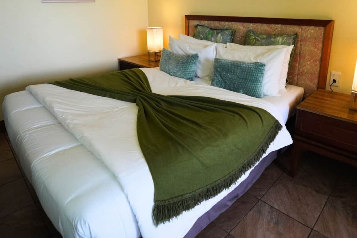 A double bed with a green throw blanket, two bedside tables with lamps, and two framed pictures on the walls.