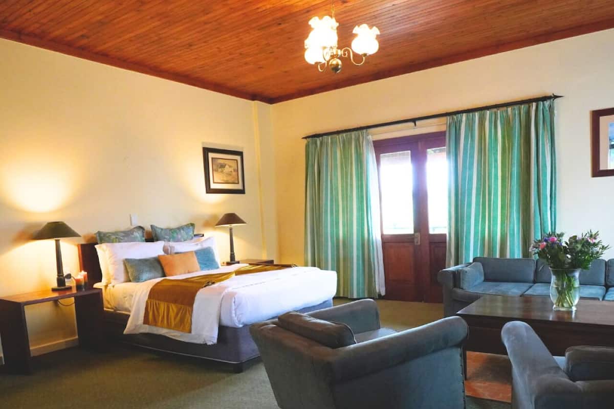 A hotel room with a wooden ceiling, a bed with a white comforter, two bedside tables with lamps, a sofa, and a coffee table.