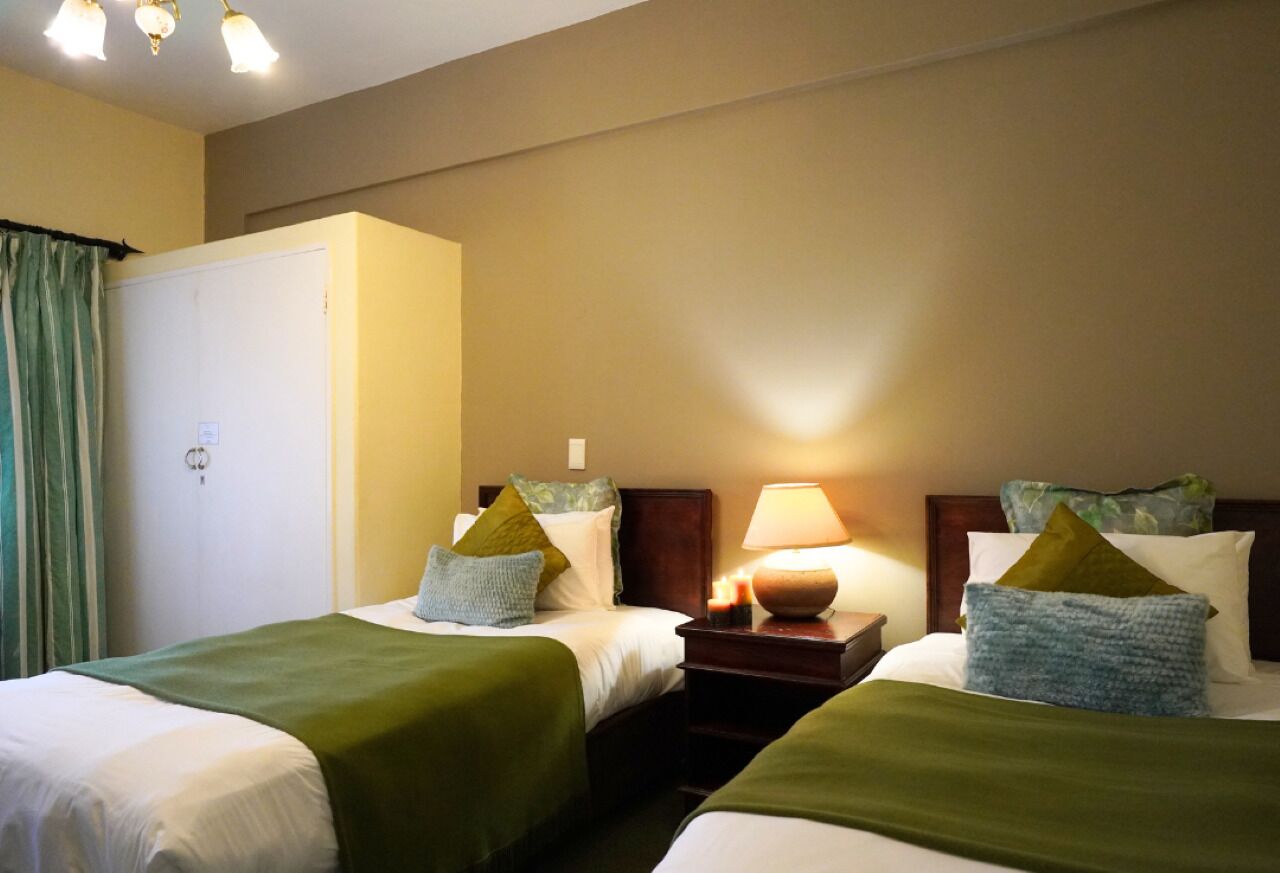 A hotel room with two beds, a nightstand with a lamp, and a wardrobe.