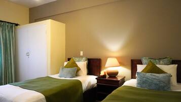 A hotel room with two beds, a nightstand with a lamp, and a wardrobe.