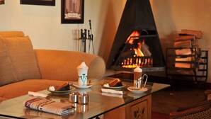 A cozy living room with a fireplace, a sofa, and a table with a newspaper, a cup, and a plate of food.
