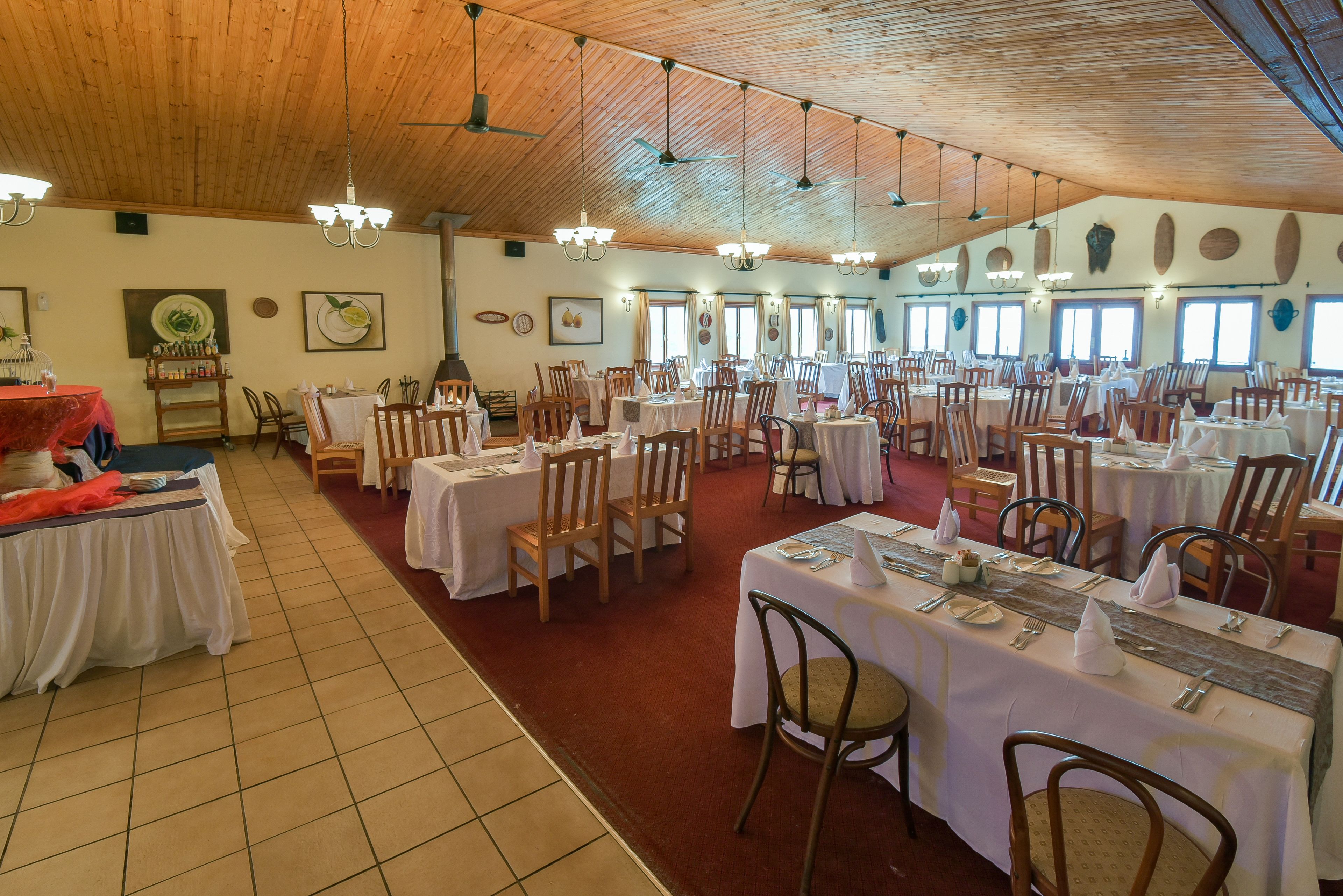 A large dining hall with multiple tables set for a meal, wooden ceiling, and artwork on the walls.