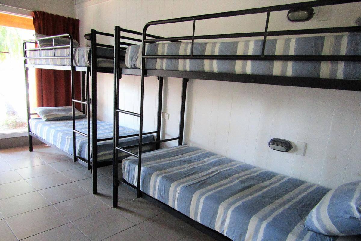 A dormitory room with bunk beds, a window with curtains, and a tiled floor.