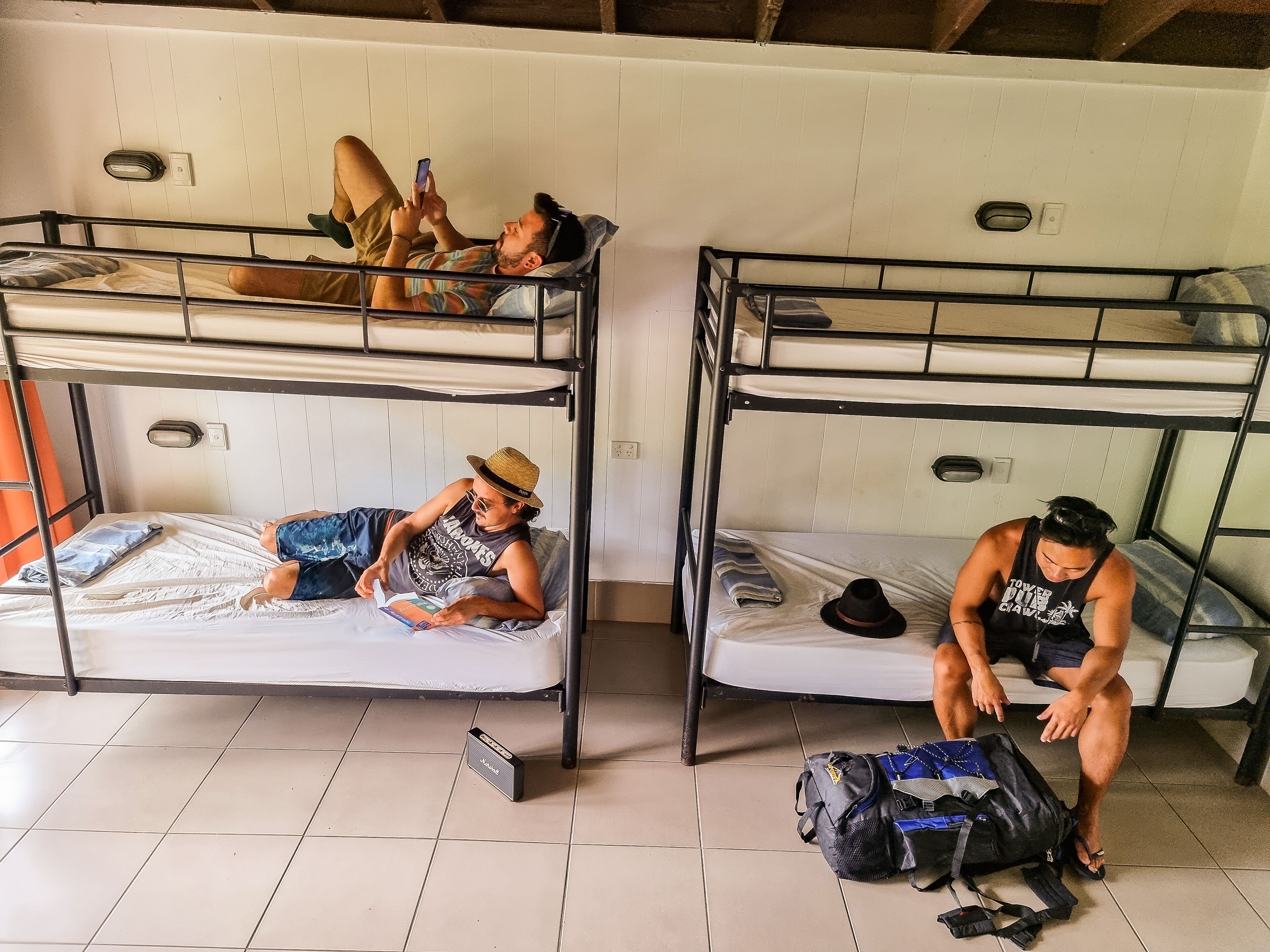 A dormitory room with bunk beds, a tiled floor, and a suitcase on the floor.
