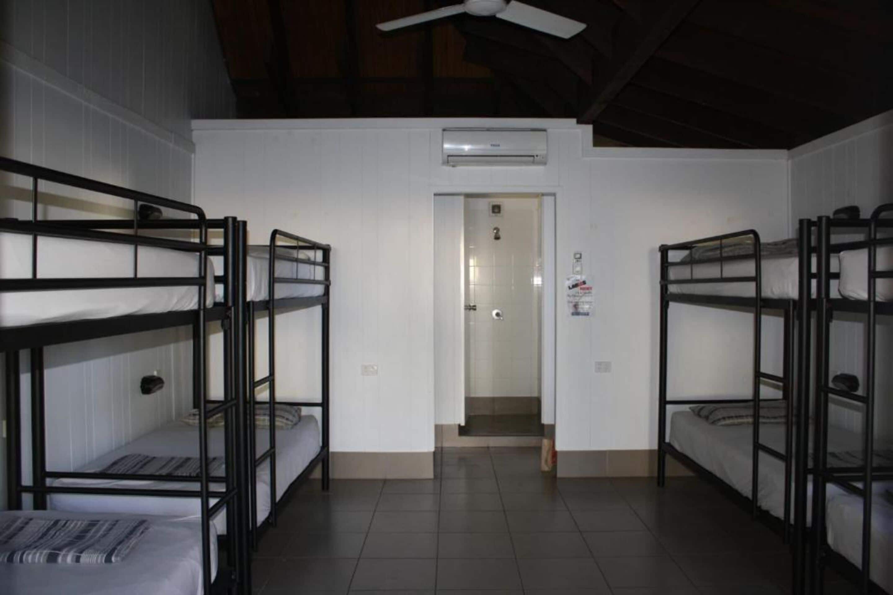A dormitory room with bunk beds, a ceiling fan, and an air conditioning unit.