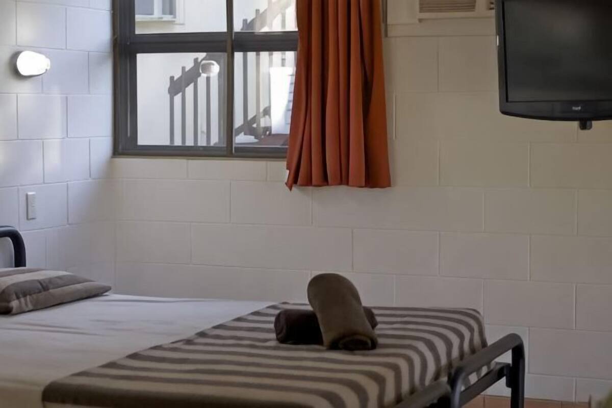 A single bed with a striped bedspread, a rolled towel, and a pillow.