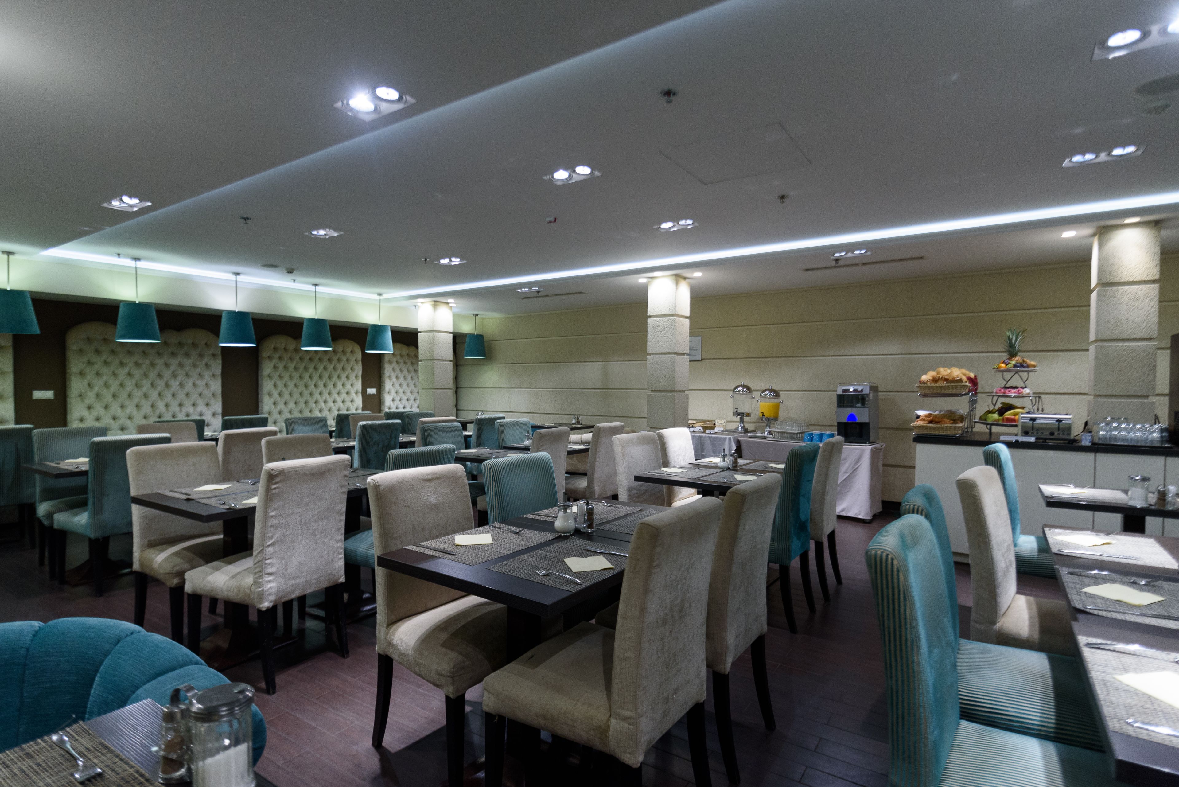A restaurant with multiple dining tables and chairs, a kitchen area, and a buffet with various food items.