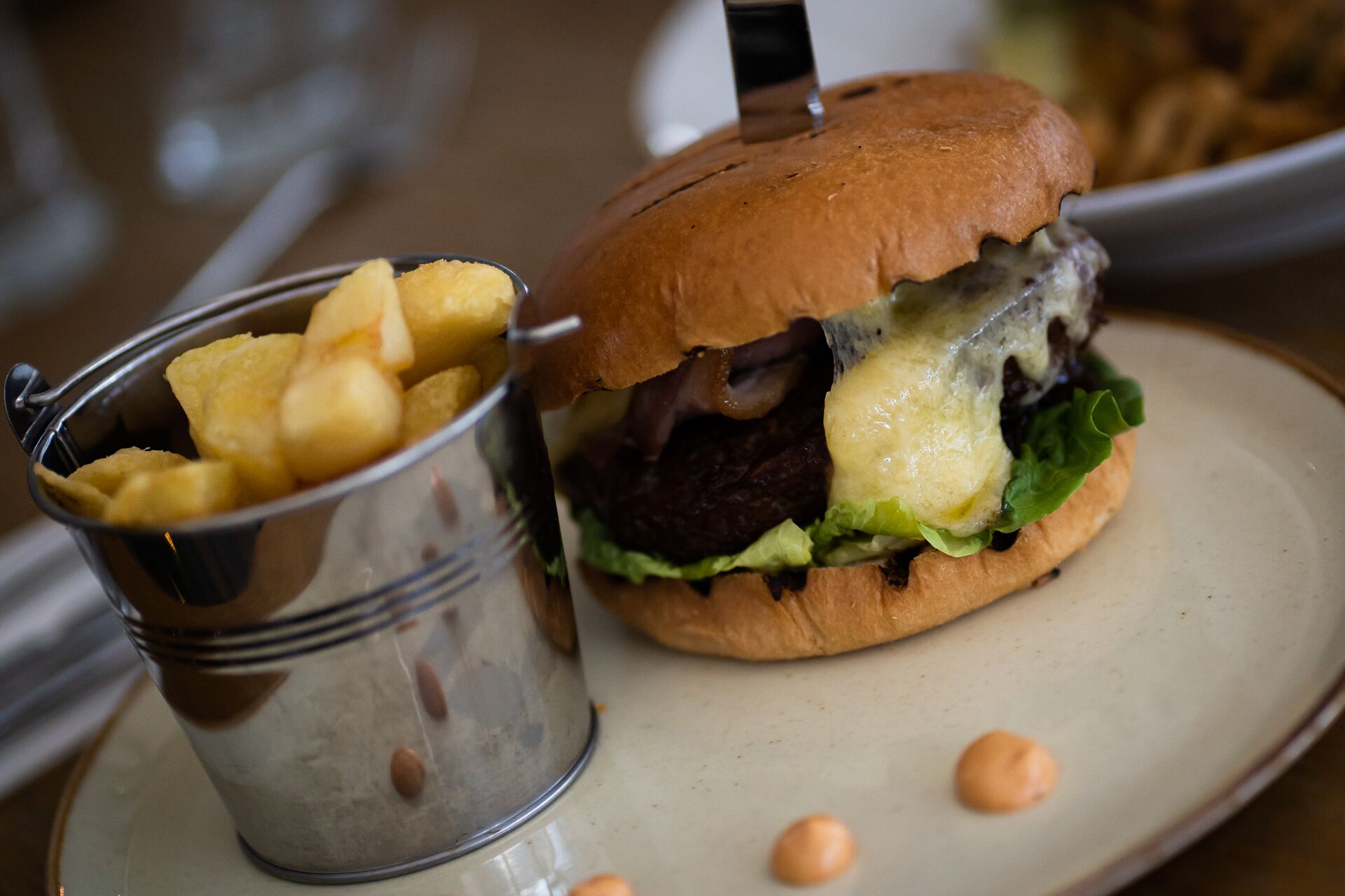 En burger med bolle, salat, ost og pommes frites i et metalglas.