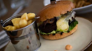 Una hamburguesa con pan, lechuga, queso y una porción de papas fritas en un vaso de metal.