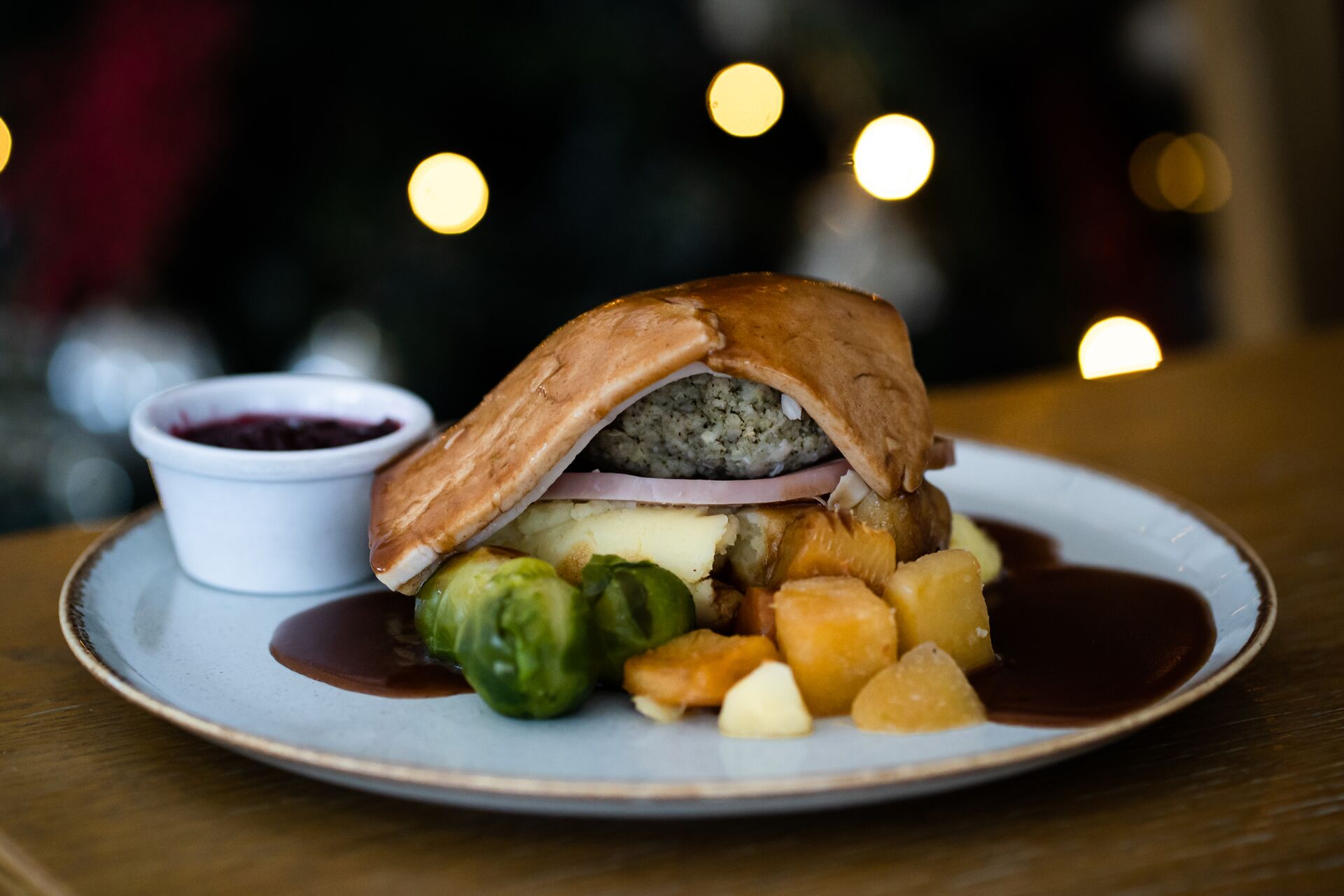 A plate with a sandwich, Brussels sprouts, and a small bowl of sauce.