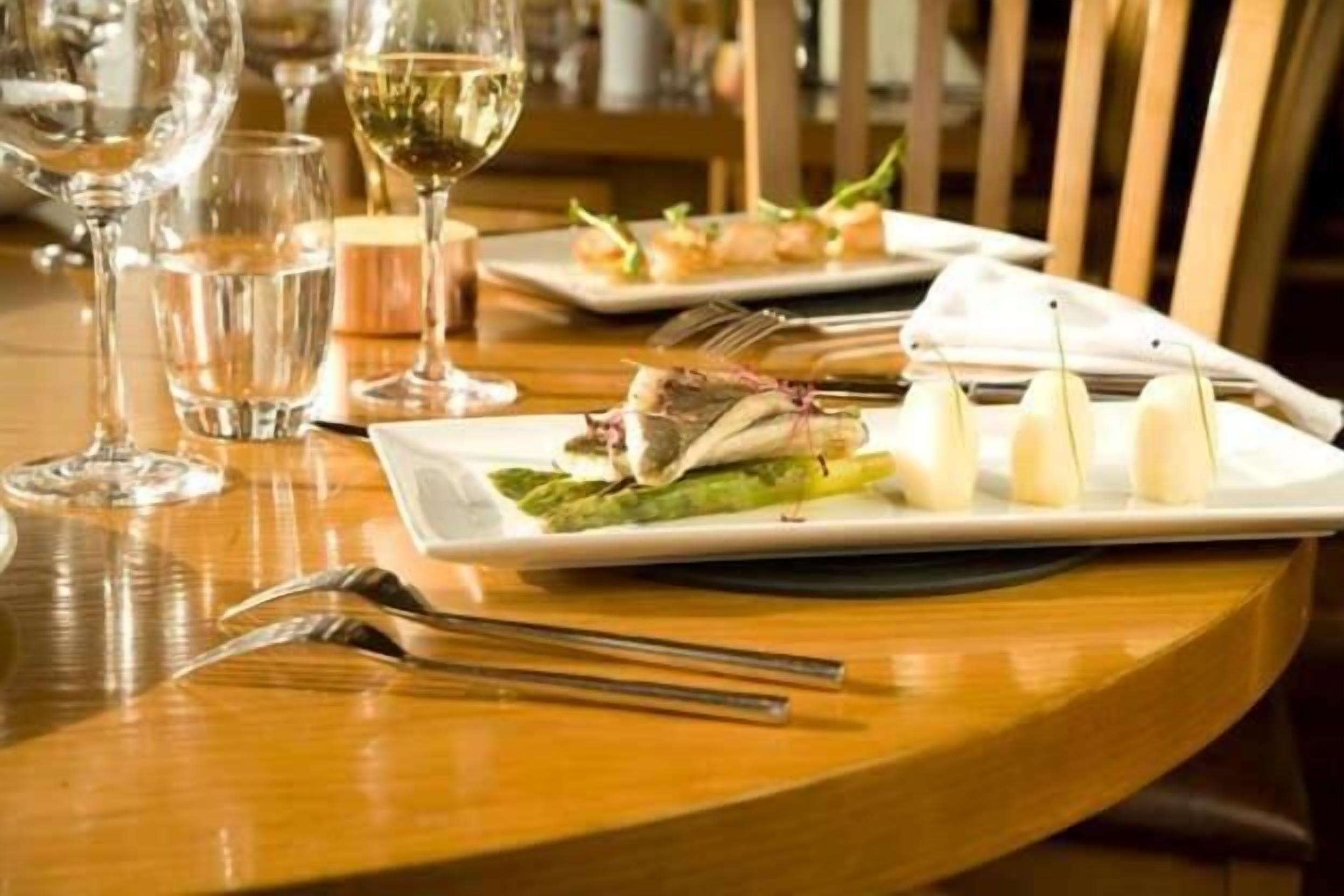 A dining table with plates of food, wine glasses, and cutlery.