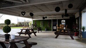 An outdoor patio area with picnic tables, potted plants, and decorative elements like hanging lights and a heart-shaped decoration.