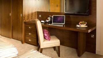 Un dormitorio con cama, escritorio con computadora portátil, televisor y armario.