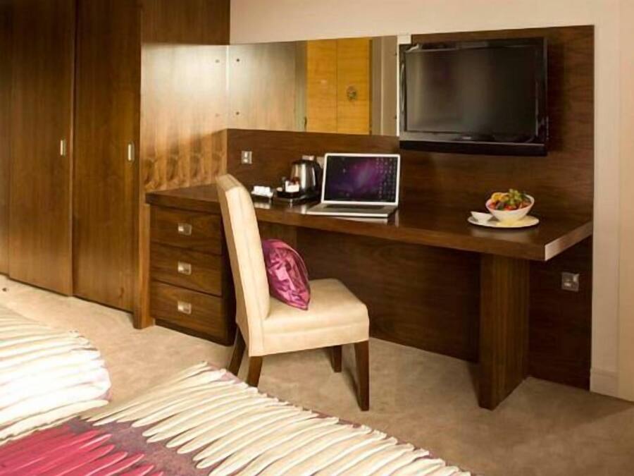 Un dormitorio con cama, escritorio con computadora portátil, televisor y armario.