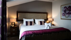 A hotel room with a large bed, two bedside lamps, a telephone, a nightstand, and a framed floral artwork on the wall.