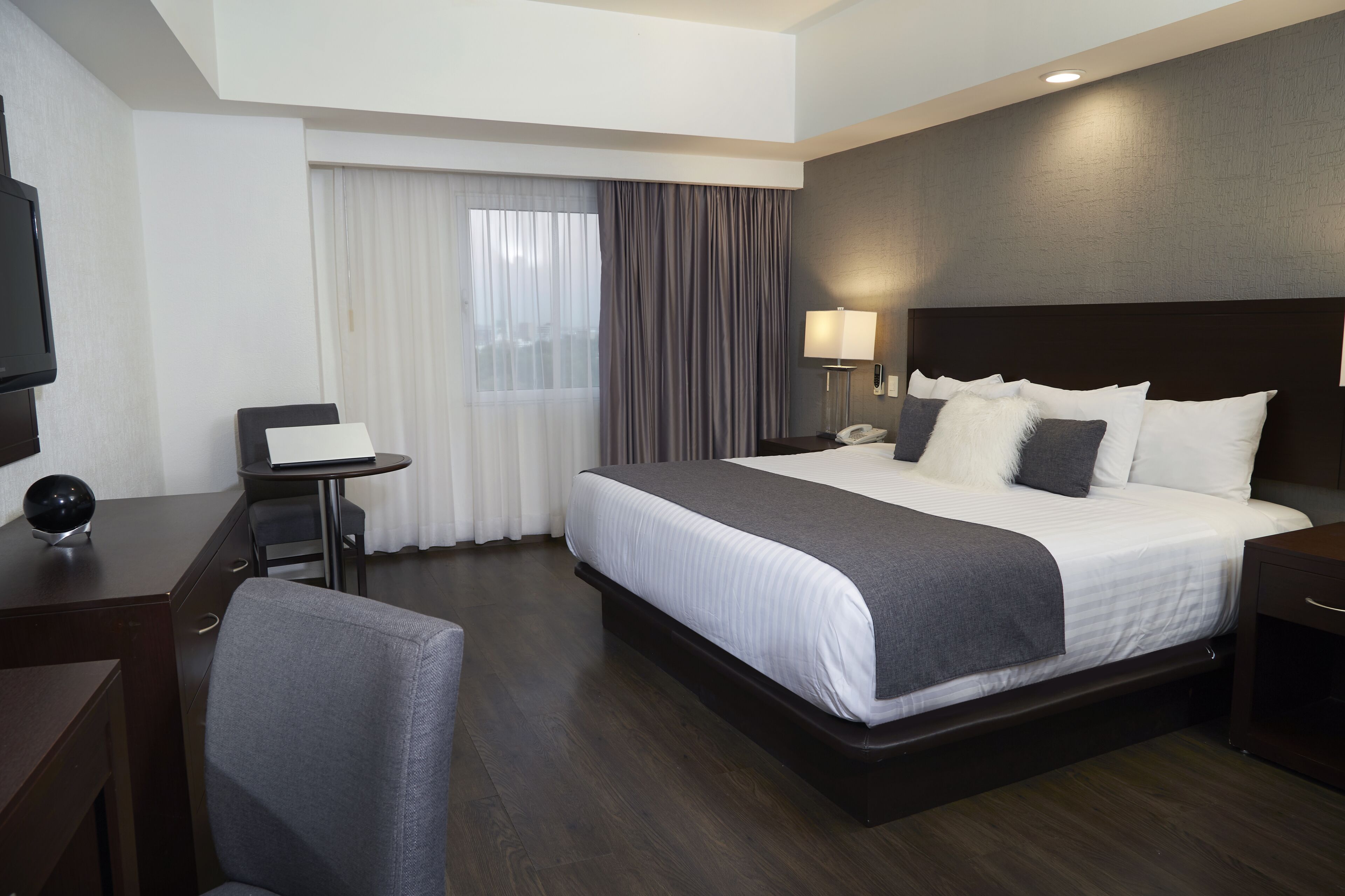 A hotel room with a large bed, a desk with a chair, a TV, and a window with curtains.