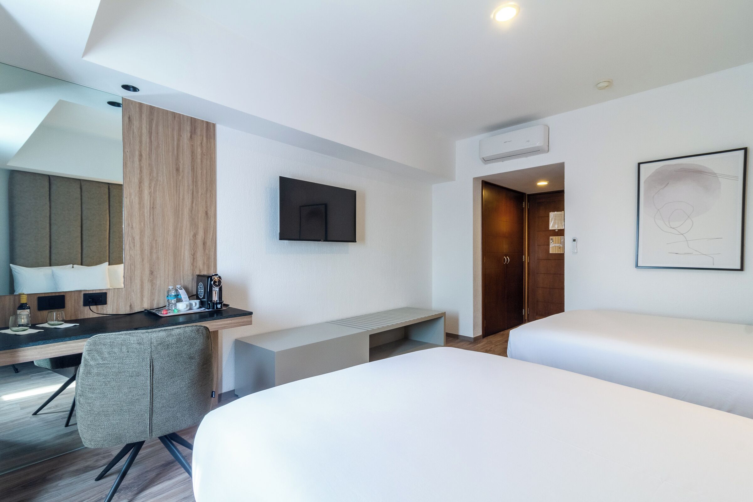 Ein modernes Hotelzimmer mit Schreibtisch, zwei Betten, einem Wand-Fernseher und einem großen Fenster.
