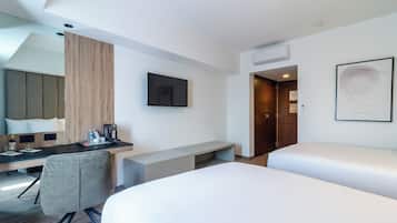 Ein modernes Hotelzimmer mit Schreibtisch, zwei Betten, einem Wand-Fernseher und einem großen Fenster.