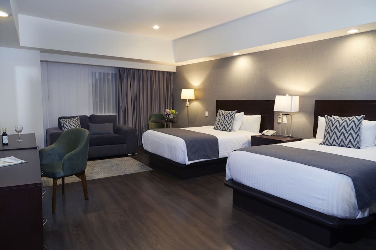 Una habitación de hotel con dos camas, un escritorio, una silla y una lámpara.