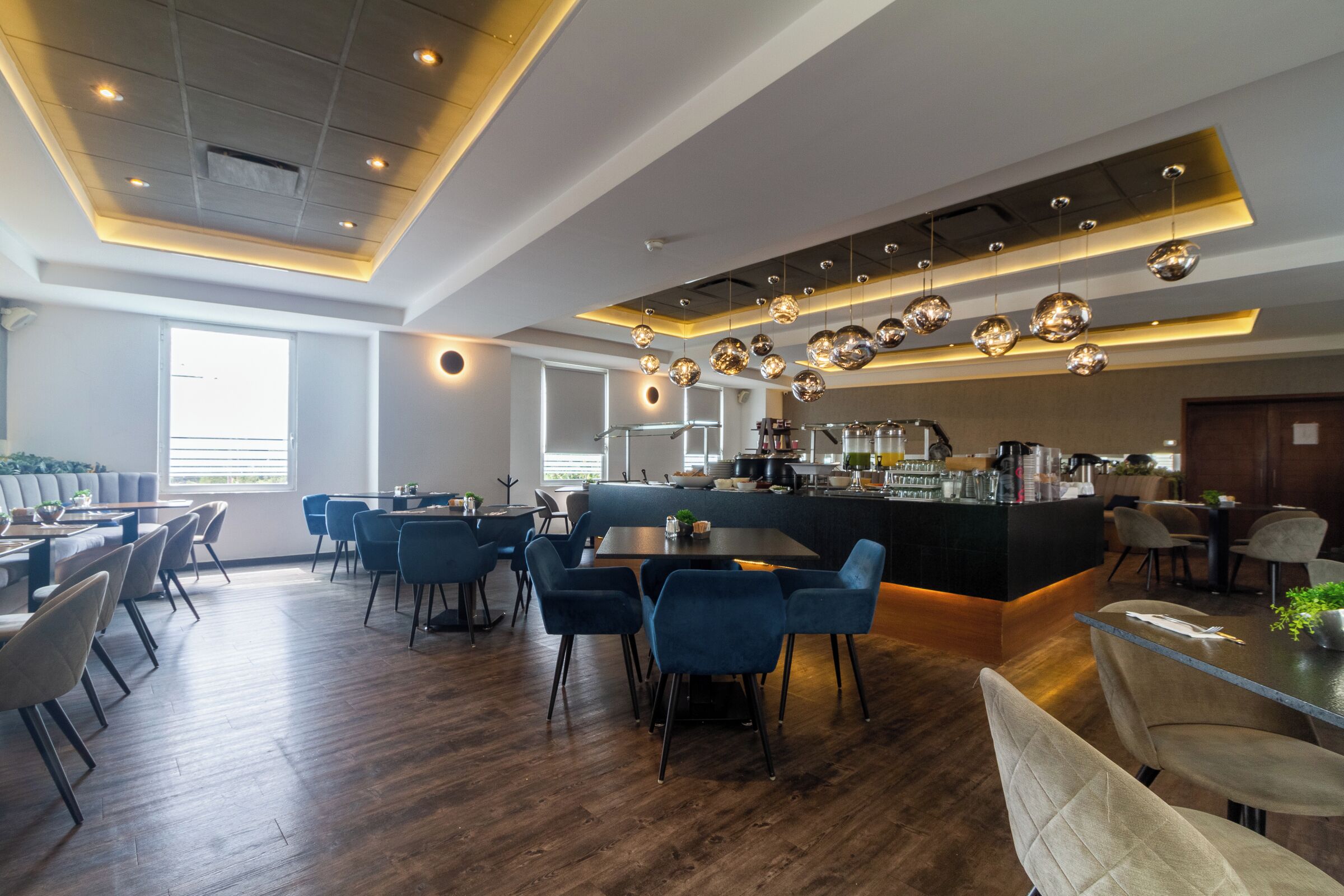 Un restaurante moderno con zona de bar, suelo de madera y sillas azules.