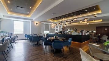 Een modern restaurant met een bar, houten vloeren en blauwe stoelen.