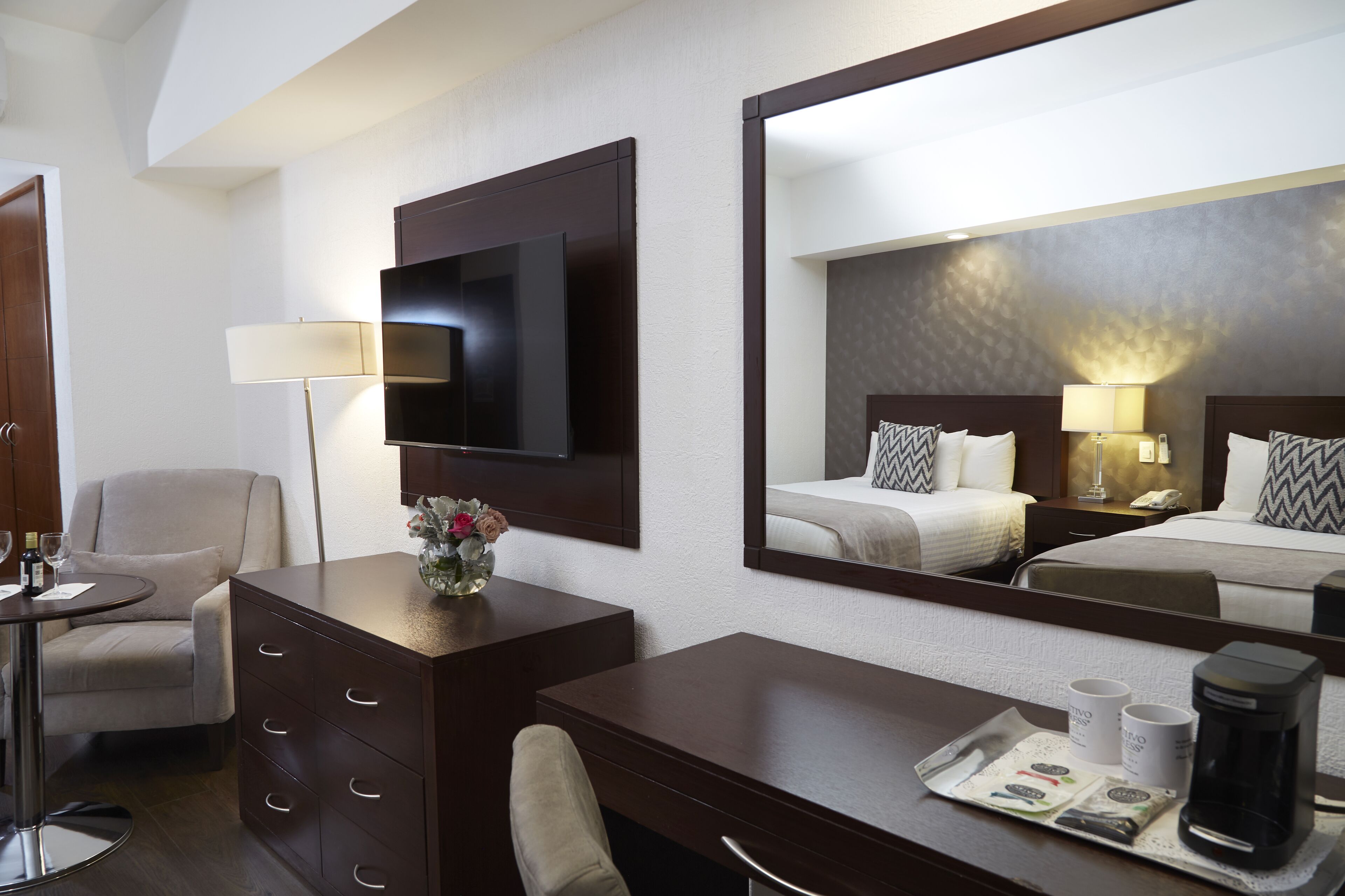 A hotel room with a bed, a desk, a chair, a TV, a lamp, and a coffee maker.