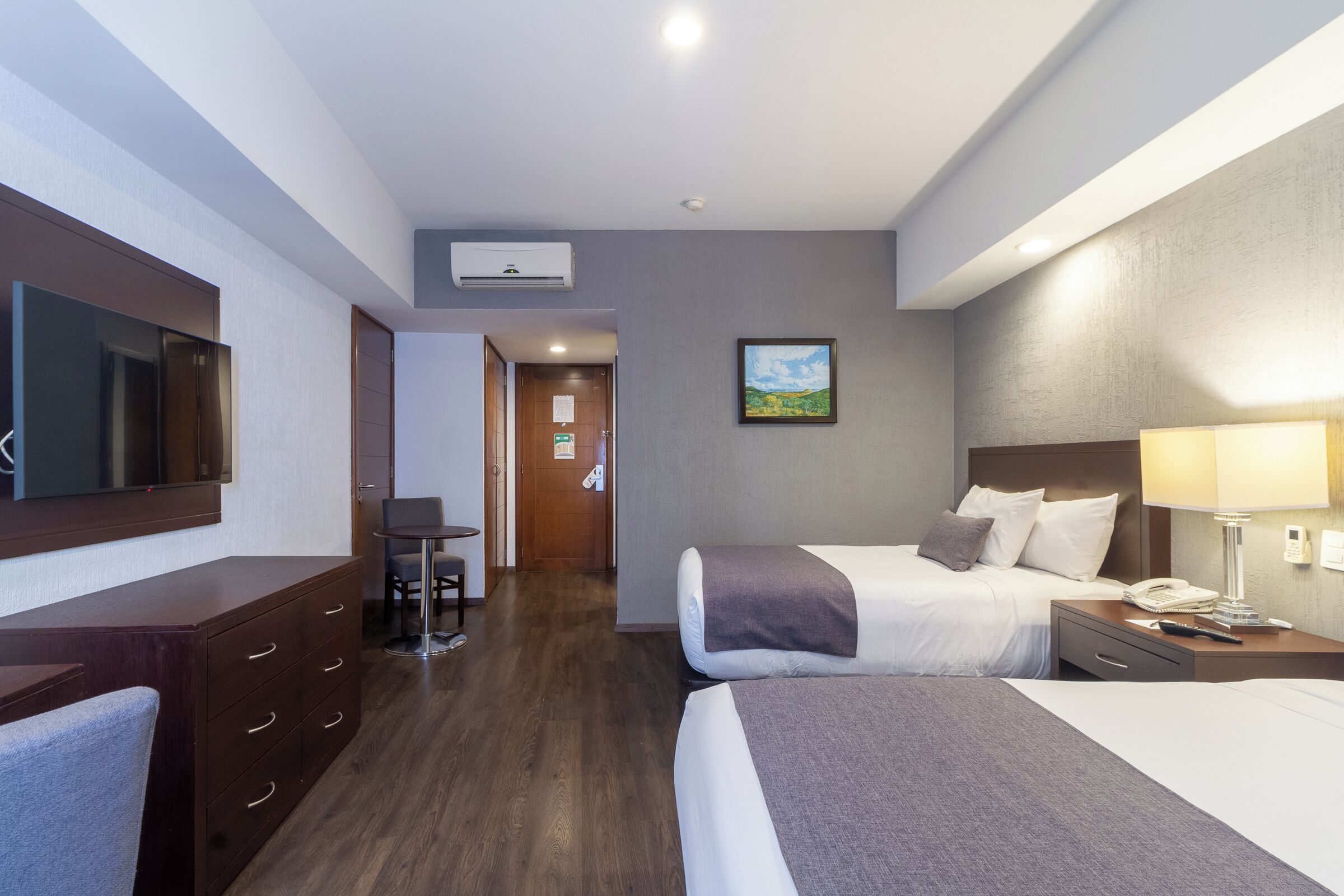 A hotel room with a bed, bedside table, lamp, and a TV on the wall.