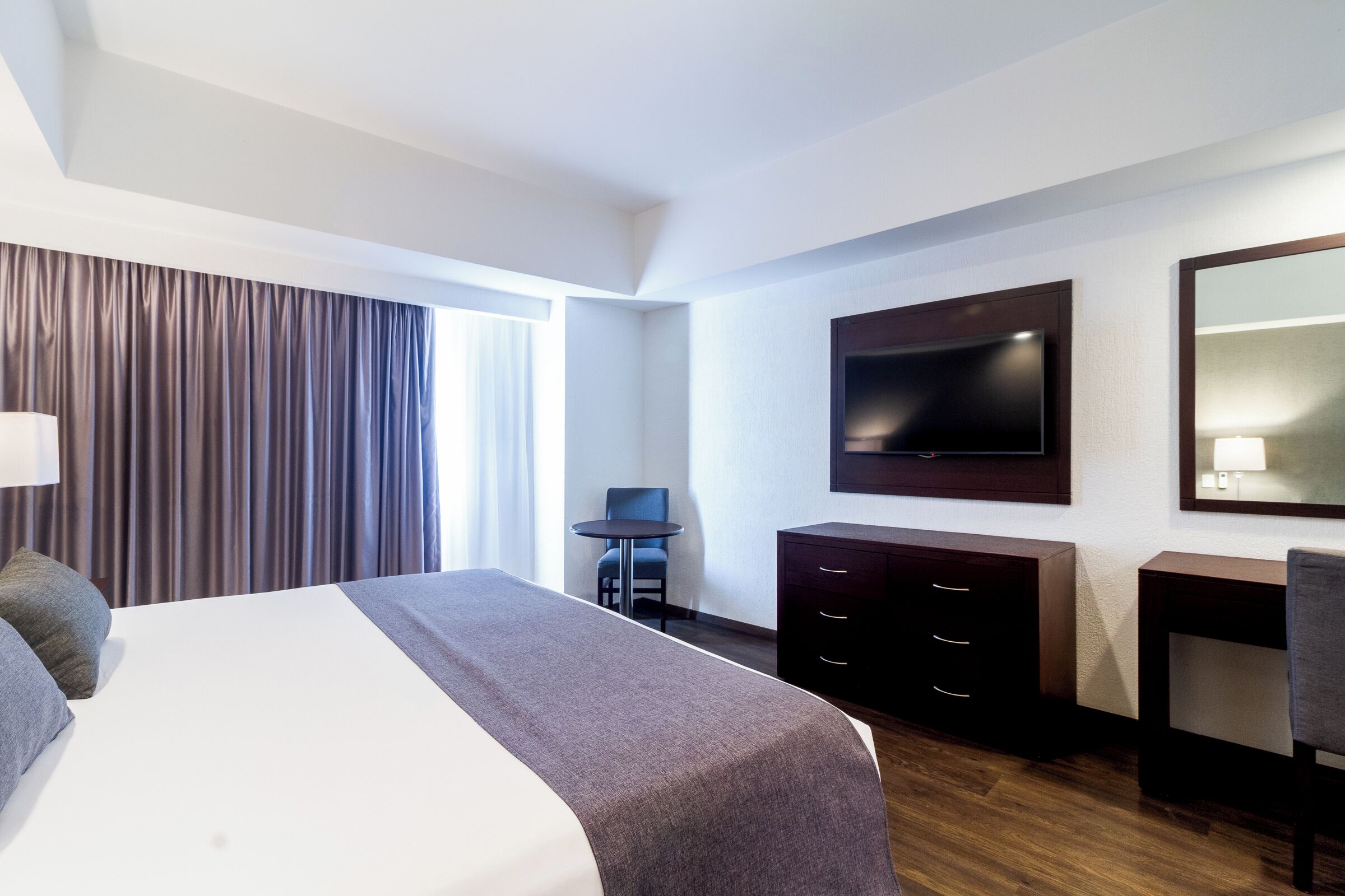 Een hotelkamer met een groot bed, een aan de muur bevestigde televisie, een bureau en een stoel.