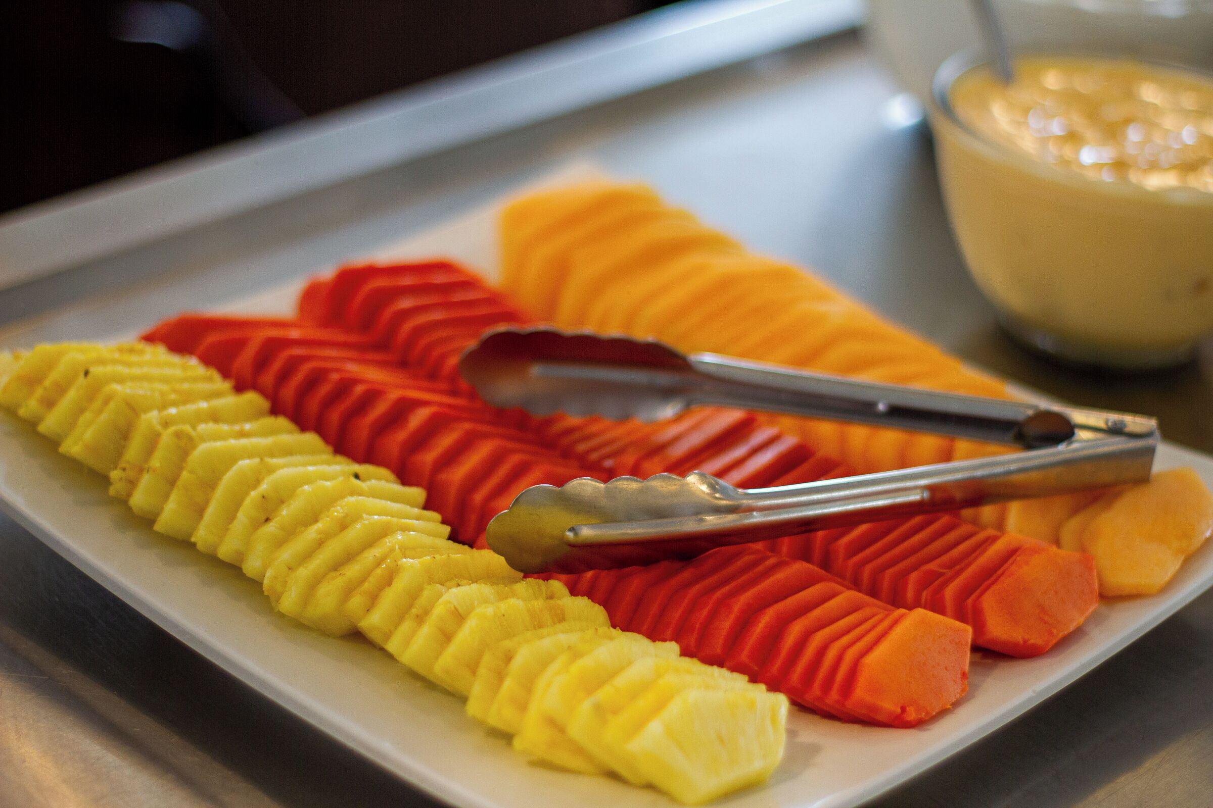 Un plat amb talls perfectes d'anana i mango, acompanyats d'unes pinces.