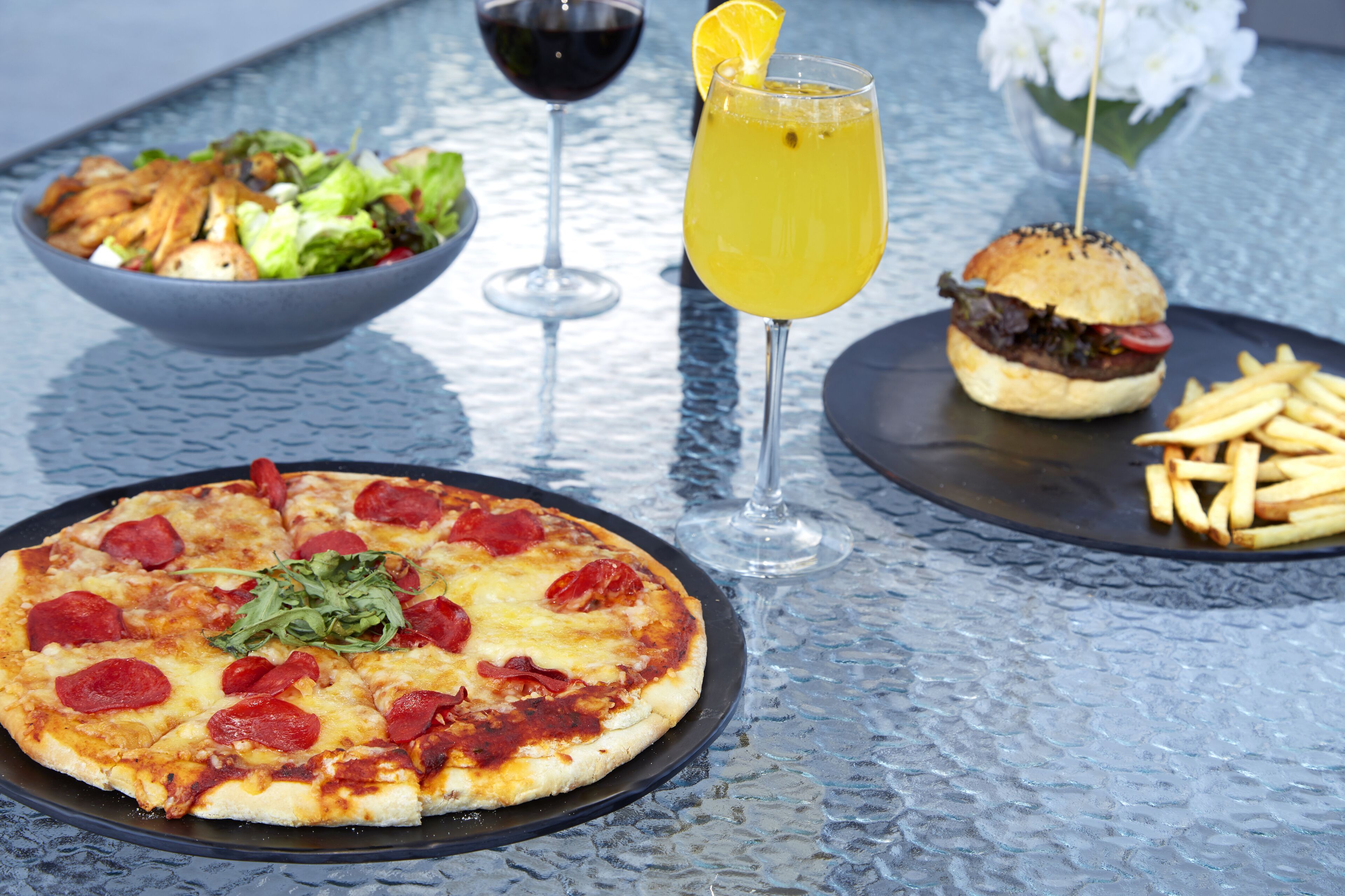 A pizza, a burger, fries, a salad, and a drink on a table.