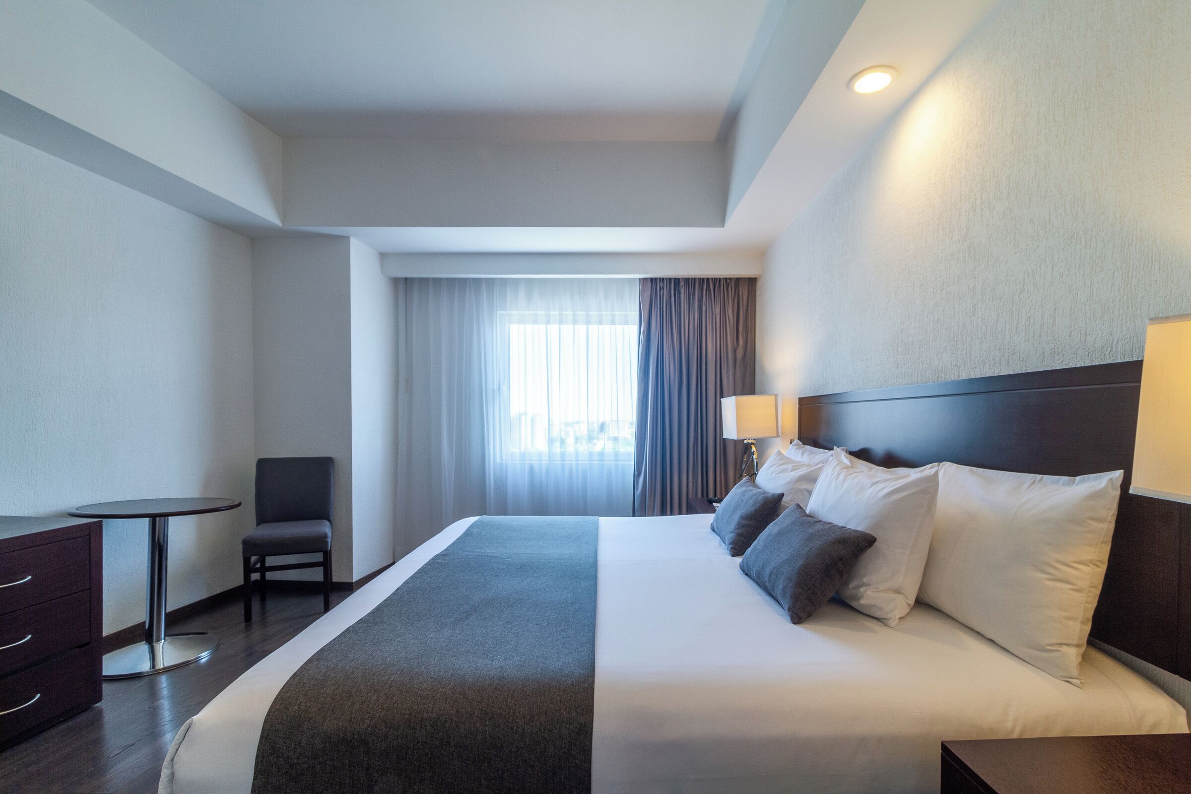 A hotel room with a bed, a desk, a chair, and a window with curtains.