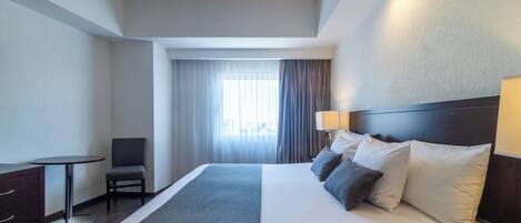 Ein Hotelzimmer mit einem Bett, einem Schreibtisch, einem Stuhl und einem fenster mit Vorhängen.