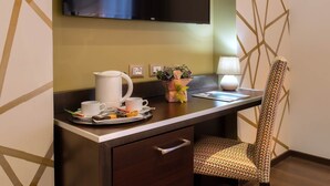 A hotel room with a desk, a television mounted on the wall, a chair, a lamp, and a tray with breakfast items. - Infinity Hotel San Pietro (Rome)