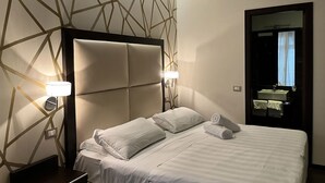 A hotel room with a modern geometric wall design, a large bed with white linens, two bedside lamps, and a visible bathroom mirror. - Infinity Hotel San Pietro (Rome)