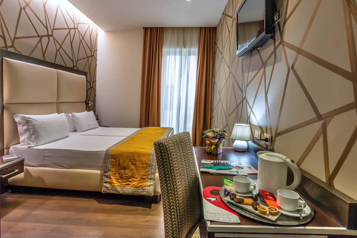 A hotel room with a bed, a desk with a tray of breakfast items, a lamp, and a window with curtains.